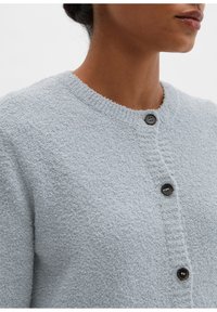 Hellgraue Strickjacke aus strukturiertem Stoff, mit rundem Kragen, vier schwarzen Knöpfen und gerippten Details entlang der Kanten.