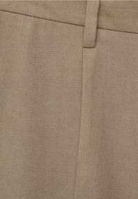 Gros plan sur un tissu beige avec un motif de tissage diagonal, présentant une passant de ceinture et un détail de couture sur un vêtement.