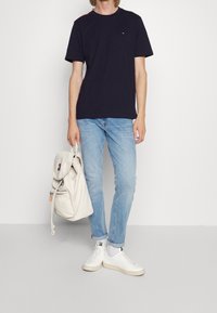 Granatowy bawełniany t-shirt z okrągłym dekoltem i czerwonymi akcentami na ramionach, w połączeniu z jasnoniebieskimi dżinsami i białym plecakiem. Białe trampki.