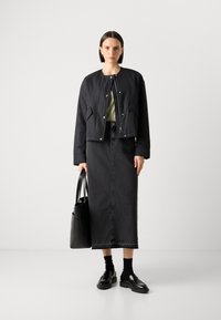 Černá zkrácená bomber bunda, olivově zelený top, černá džínová midi sukně, černá kabelka, černé ponožky a lesklé černé mokasíny. Jednoduchý design.