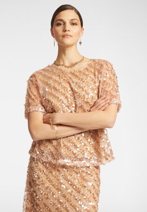 Roze gouden top met pailletten en korte mouwen, met een losse fit en een gestructureerd oppervlak. Gecombineerd met een bijpassende paillettenrok. Gouden sieraden accenten.