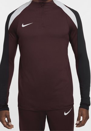 Homme portant un haut de sport Nike à manches longues bordeaux et noir avec des logos swoosh blancs sur la poitrine et le pantalon.