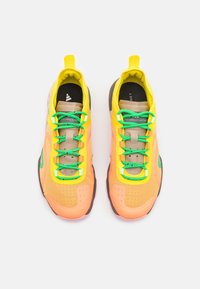 Tenisky s vrškem z prodyšné síťoviny a syntetického materiálu v oranžové, žluté a zelené barvě. Mají zelené tkaničky, polstrovaný límec a texturovanou podrážku pro lepší grip.