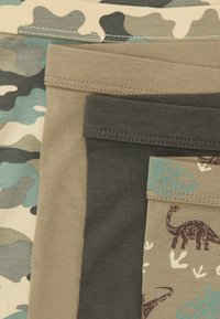 Cuatro pares de leggings para niños: estampado de camuflaje, caqui, verde oscuro y beige con dibujos de dinosaurios. Mezcla de algodón, con diferentes texturas y colores.