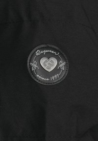 Tela negra con un parche circular de cuero oscuro con un corazón plateado en relieve y el texto "Desde 1997" con acentos decorativos de hojas.