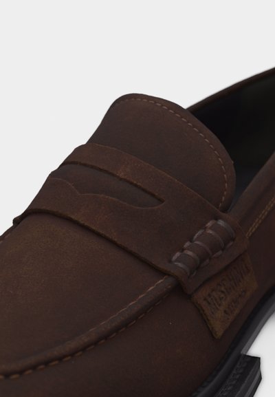 Mocassin en cuir marron avec coutures moc toe, bride penny et étiquette de marque sur une semelle foncée, sur fond blanc.