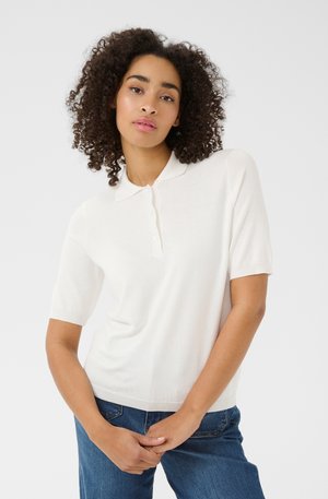 Creme korte mouwen polo shirt gemaakt van zacht materiaal, met een klassieke kraag, knoopsluiting en ribgebreide zoom, gedragen met blauwe spijkerbroek.