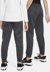 Donkergrijze joggingbroek met een tapers ontwerp, elastische tailleband en geribde boorden, gecombineerd met zwarte sportschoenen.