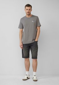 Szary t-shirt z krótkim rękawem i okrągłym dekoltem, ozdobiony małym detalem graficznym, w połączeniu z ciemnoniebieskimi szortami dżinsowymi i białymi sneakersami z szarymi akcentami.