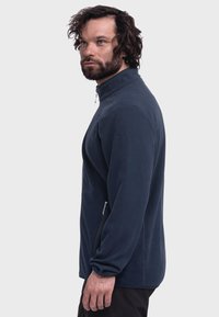 Navy fleece jacket with a high collar, zippered pockets on the sides, and elastic cuffs. Soft texture and minimalistic design.