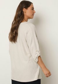 Lichtbeige pullover met een geribbelde textuur, driekwartmouwen en opgerolde manchetten. Losse pasvorm met een iets gebogen zoom.
