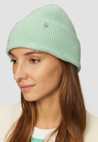 Lichtgroene geribbelde beanie met een kleine decoratieve zilveren accent. De stof heeft een zachte, gestructureerde uitstraling en loopt taps toe naar de kroon.