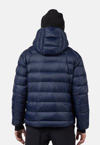 Giacca imbottita blu navy con sezioni cucite orizzontalmente e cappuccio. Presenta una texture liscia e polsini a costine.