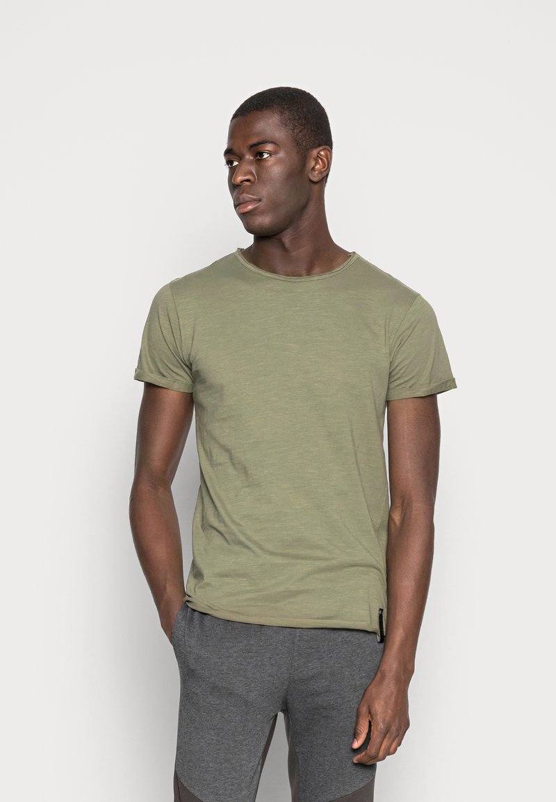 Oliven grøn crew-neck t-shirt i let stof, med korte ærmer og en afslappet pasform, parret med grå atletiske shorts.