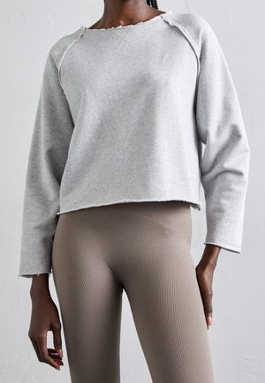 Person wearing a light gray cropped sweatshirt with frayed edges and high-waisted ribbed taupe leggings against a plain background.