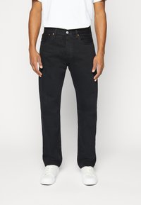 Jeans de mezclilla negros con corte recto, que cuentan con cinco bolsillos y cierre de botón metálico. Combinados con zapatillas blancas y una camiseta blanca básica.