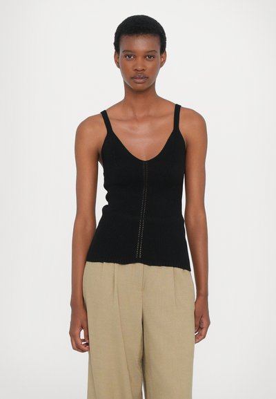 Schwarzes geripptes Tanktop mit V-Ausschnitt, ausgestattet mit dünnen Trägern und einem dezenten vertikalen Streifenmuster in der Mitte. Kombiniert mit beigen Hosen.