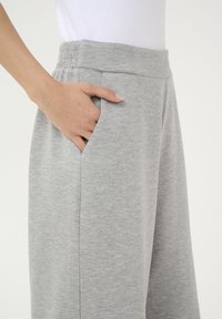Grå bomullsblandade byxor med vida ben, featuring midja med elastisk band och sidofickor. Slät textur och minimalistisk stil.