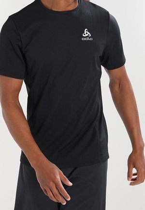 Hombre con una camiseta deportiva de manga corta negra lisa con un logo blanco de Odlo en el pecho, parte superior izquierda.