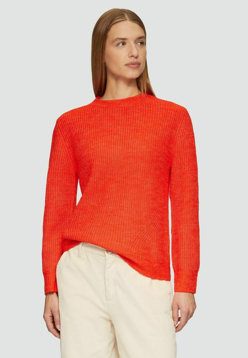Helle orange gestrickte Pullover mit strukturiertem Muster, rundem Ausschnitt und langen Ärmeln. Kombiniert mit hellen Hosen.