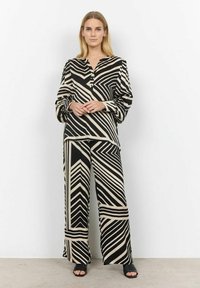 Zwart en beige gestreept outfit met een knoopsluiting aan de voorkant, lange mouwen en broek met wijde pijpen, beide met geometrische patronen.