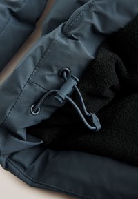 Fabric close-up of a dark blue jacket cuff with an adjustable drawstring and black fleece lining visible inside.