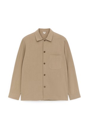 Ilgas smėlio spalvos marškiniai su sagomis, apykakle, kairėje pusėje viena krūtinės kišenė ir priekyje smėlio spalvos sagos.