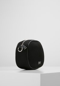 Zwarte mesh tas met een afgeronde vorm, ritsafsluiting en metalen hardware. Heeft een gladde zwarte afwerking en een klein logo aan de voorkant.