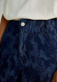 Jean en denim bleu foncé avec un motif abstrait subtil, doté d'une fermeture à bouton, passants de ceinture et poches latérales.