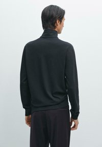 Zwarte lange mouwen pullover met een hoge kraag, met een gladde textuur en een relaxte pasvorm, gezien vanuit de achterkant.