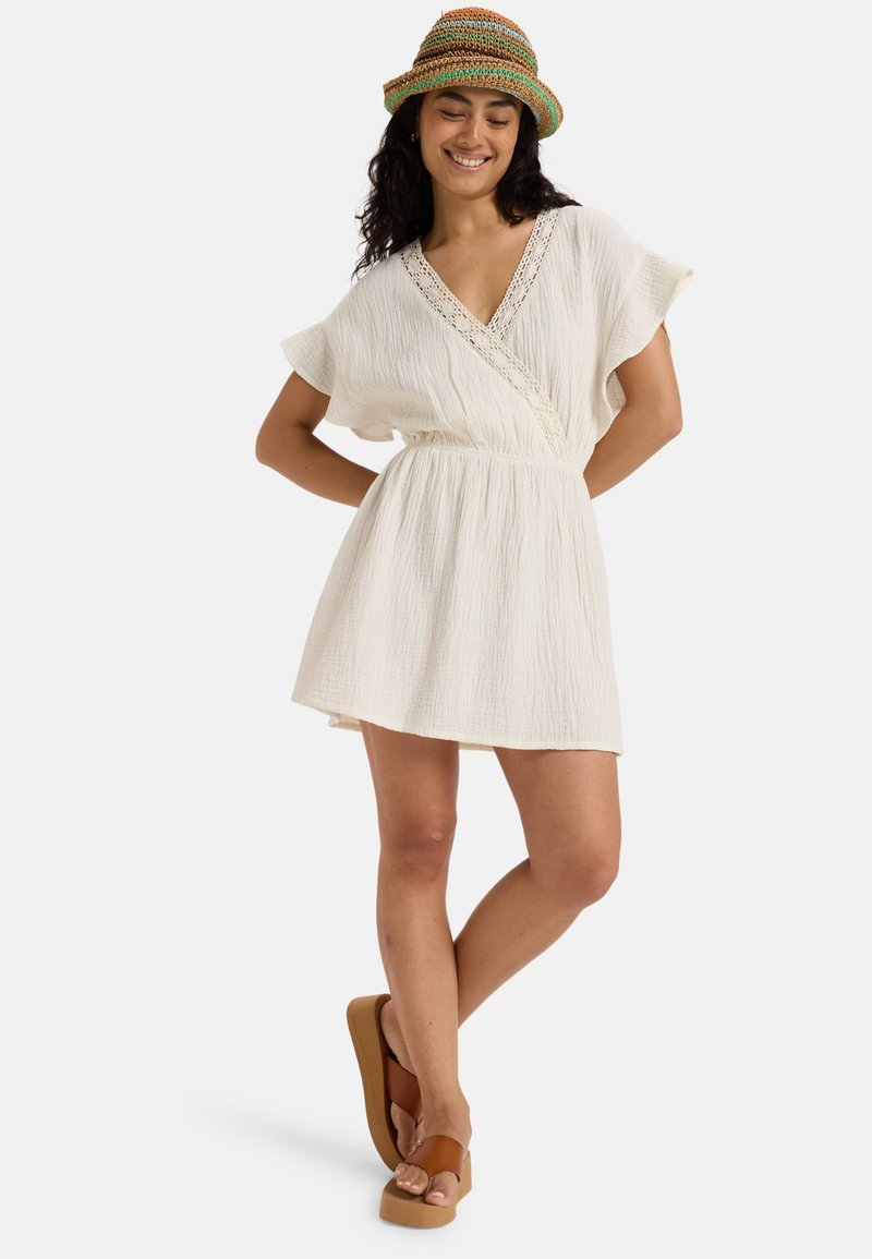 White, textured dress with a V-neck and short sleeves; cinched waist; worn with brown platform sandals; colorful woven hat.
