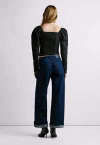 Top nero a maniche a sbuffo in tessuto testurizzato, abbinato a jeans a gamba larga blu scuro, con orli arrotolati, indossato con tacchi neri.