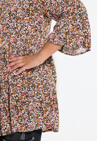 Tunika floreale con sfondo nero, caratterizzata da un motivo multicolore di piccoli fiori, maniche a campana corte e dettagli arricciati in vita.