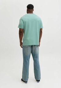 Miętowozielona koszulka z krótkim rękawem z gładkiego materiału, zestawiona z jasnoniebieskimi dżinsami o luźnym kroju, z widocznymi detalami szwów.