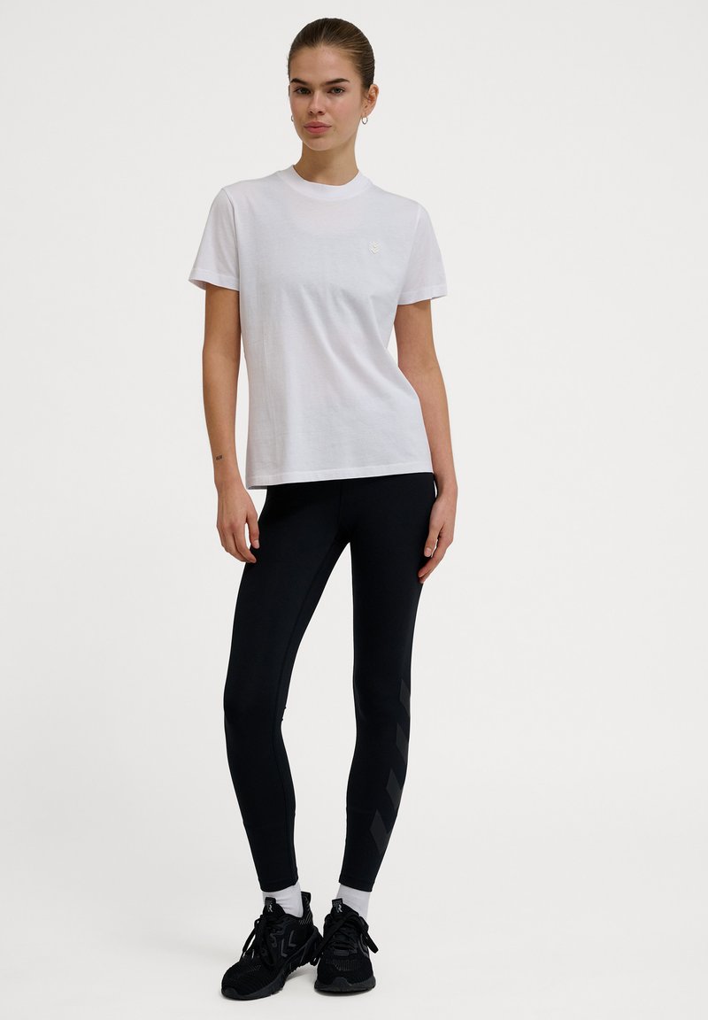 Hvid bomulds t-shirt med rund halsudskæring, parret med sorte leggings med et diagonalt stribemønster og sorte sportsko.