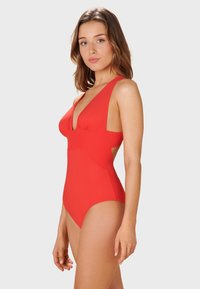 Maillot de bain rouge une pièce avec un décolleté en V plongeant, des bretelles larges et des découpes sur les côtés. Texture lisse et design ajusté pour un look épuré.