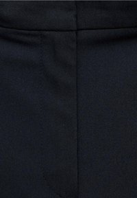 Gros plan sur un tissu bleu marine foncé avec une couture visible et le contour d'une poche sur un vêtement.