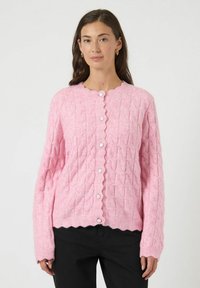 Lyserød strikket cardigan med et tekstureret kabelmønster, bølget halsudskæring og hvide knapper foran. Lange ærmer med ribstrikkede manchetter.