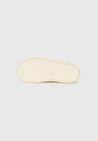 Semelle de chaussure en caoutchouc crème avec un fond texturé présentant des motifs circulaires et ondulés ; finition lisse avec le logo de la marque visible.