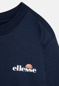 Marineblå sweatshirt med ribbestrikket krage og logo. Har en myk tekstur og et minimalistisk design. Merker seg med oransje og hvit logodetalj.