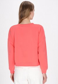 Felpa corallo dal fit morbido, con scollo rotondo e polsini a costine. Presenta un design cropped e una texture di tessuto morbido.