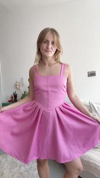 Rosa kjole med tettsittende liv, brede stropper og svakt utflared skjørt. Laget av et lett stoff med en glatt tekstur og en sentralsøm.