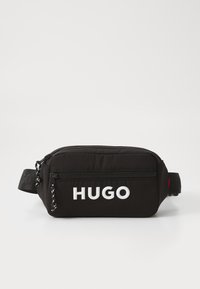 Sac banane en tissu noir avec un compartiment principal zippé, arborant un logo "HUGO" blanc et une sangle ajustable. Texture lisse avec un design minimaliste.
