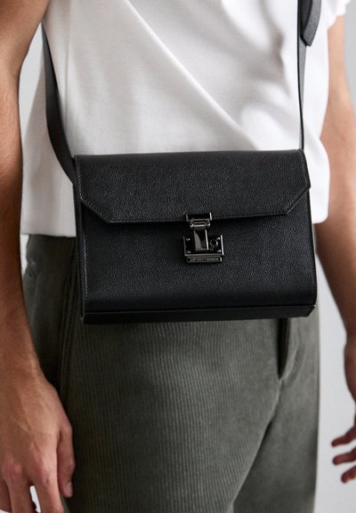 Black leather crossbody bag with a flap closure, metal clasp, and adjustable strap, featuring a textured surface and sleek rectangular shape.