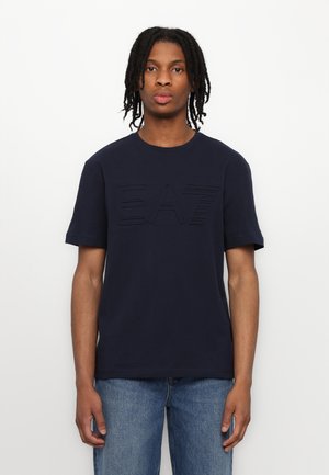 Marineblå bomuld t-shirt med korte ærmer og rund hals, med et forhøjet "EA7" logo på forsiden. Klassisk pasform.