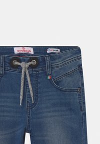 Modré slim-fit džíny s šedým stahovacím pasem, předními kapsami a malou italskou vlajkou pod páskem.