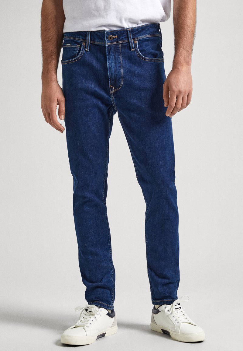 Modre jeans hlače slim kroja, z petimi žepi, kontrastnim šivanjem in zadrgo. Uporabljeni z belimi supergami.