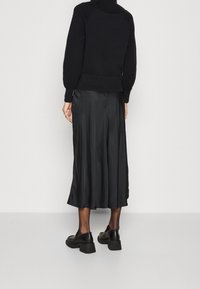 Schwarzer Strickpullover mit hochgeschlossenem Kragen, kombiniert mit einem schwarzen Satin-Midirock und klobigen schwarzen Schuhen. Glatte Textur und entspannte Passform.