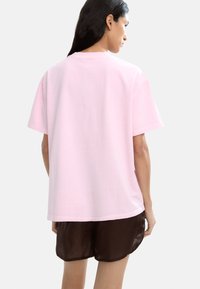 Jasnoróżowy bawełniany t-shirt o luźnym kroju, z krótkimi rękawami i okrągłym dekoltem. Materiał wydaje się miękki i gładki.