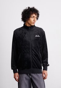 Sort velour zip-jakke med høj krave, der har sidelommer, elastiske manchetter og hvid broderet "New Era" logo på brystet.